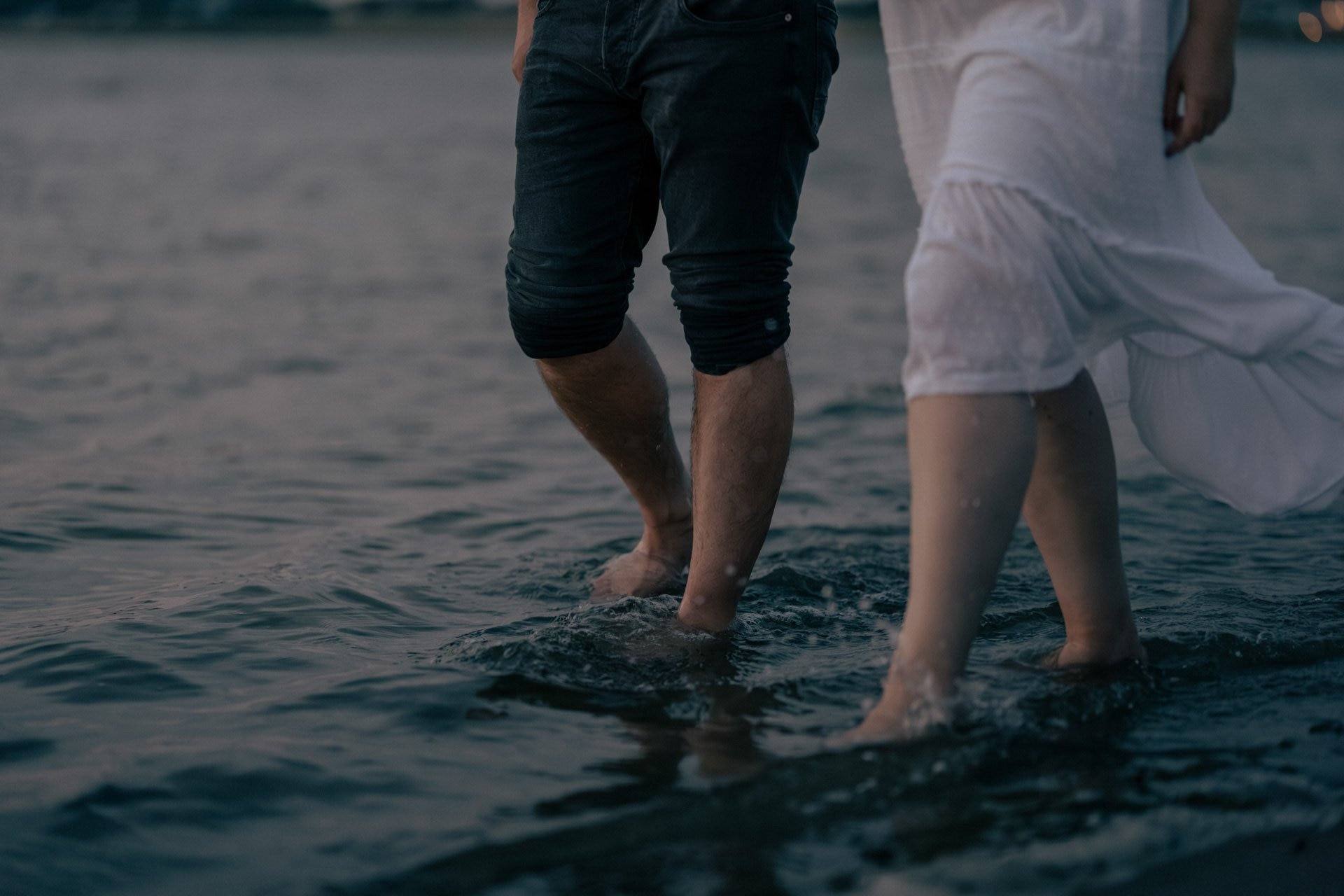 Menschen laufen barfuß im Wasser am Strand bei Sonnenuntergang.
