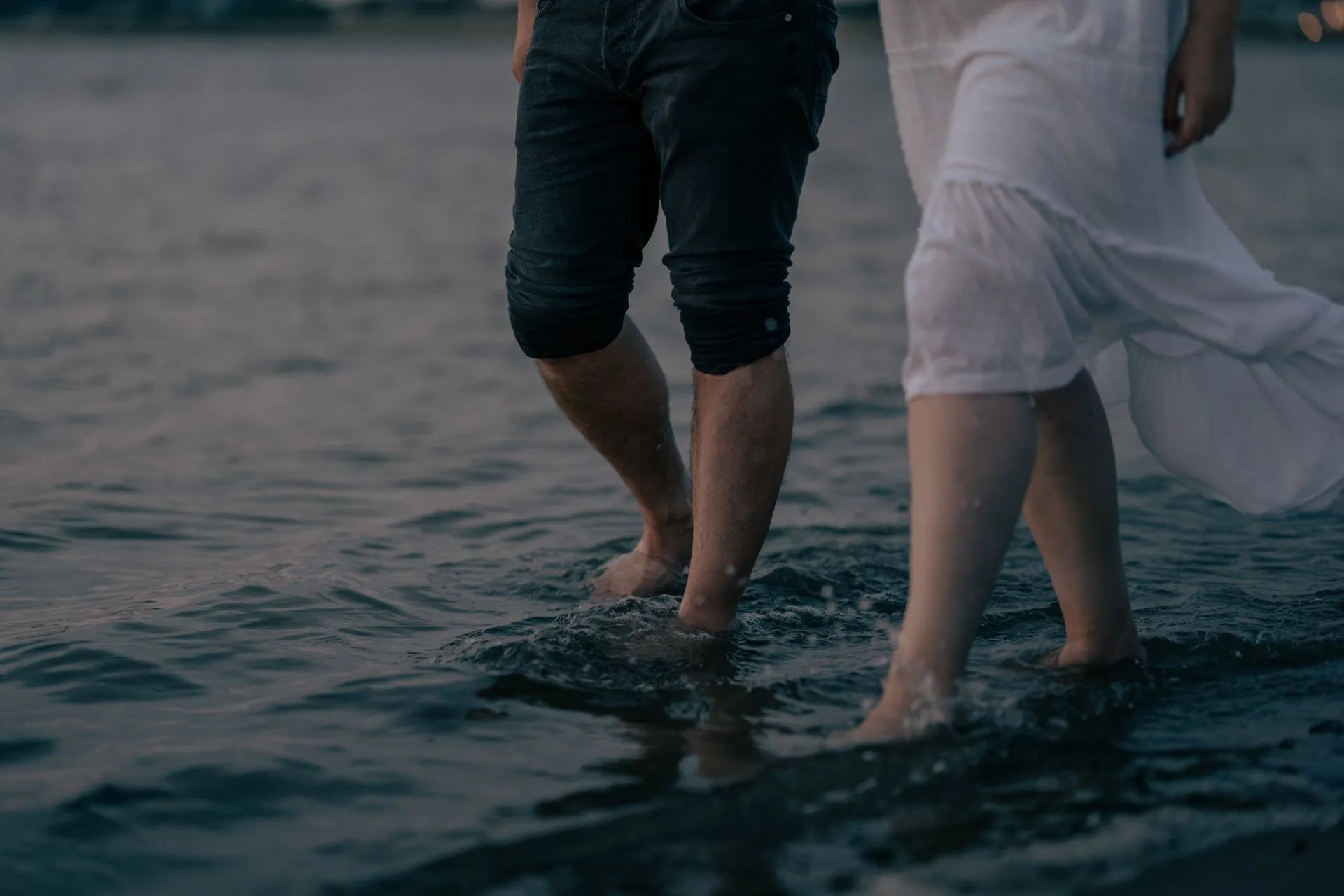Menschen laufen barfuß im Wasser am Strand bei Sonnenuntergang.