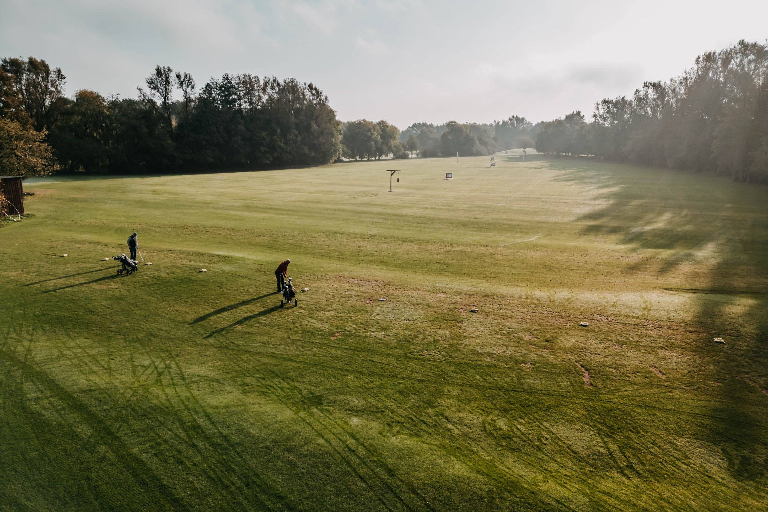 Weiter Blick über das Fairway mit zwei Golfern bei tiefstehender Sonne.