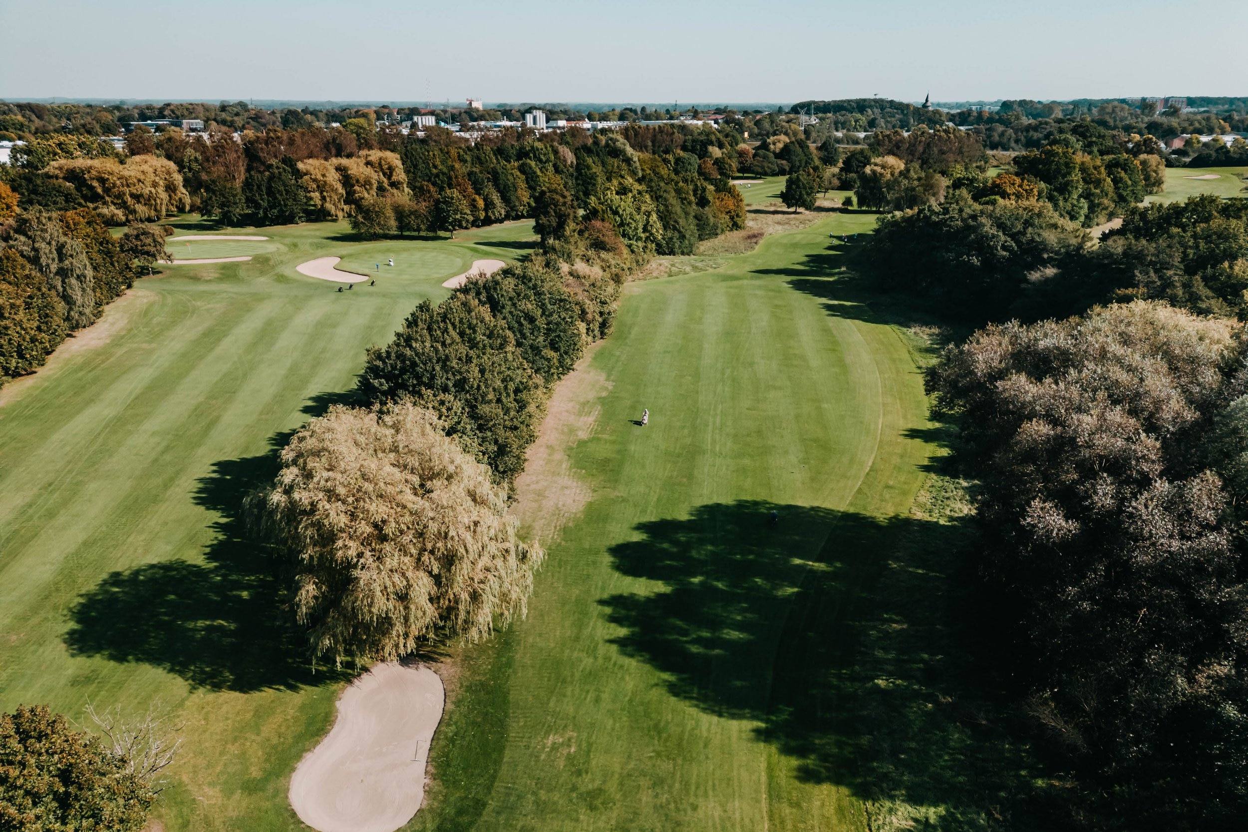 Luftaufnahme des Golfplatzes mit Fairways, Sandbunkern und Baumreihen.