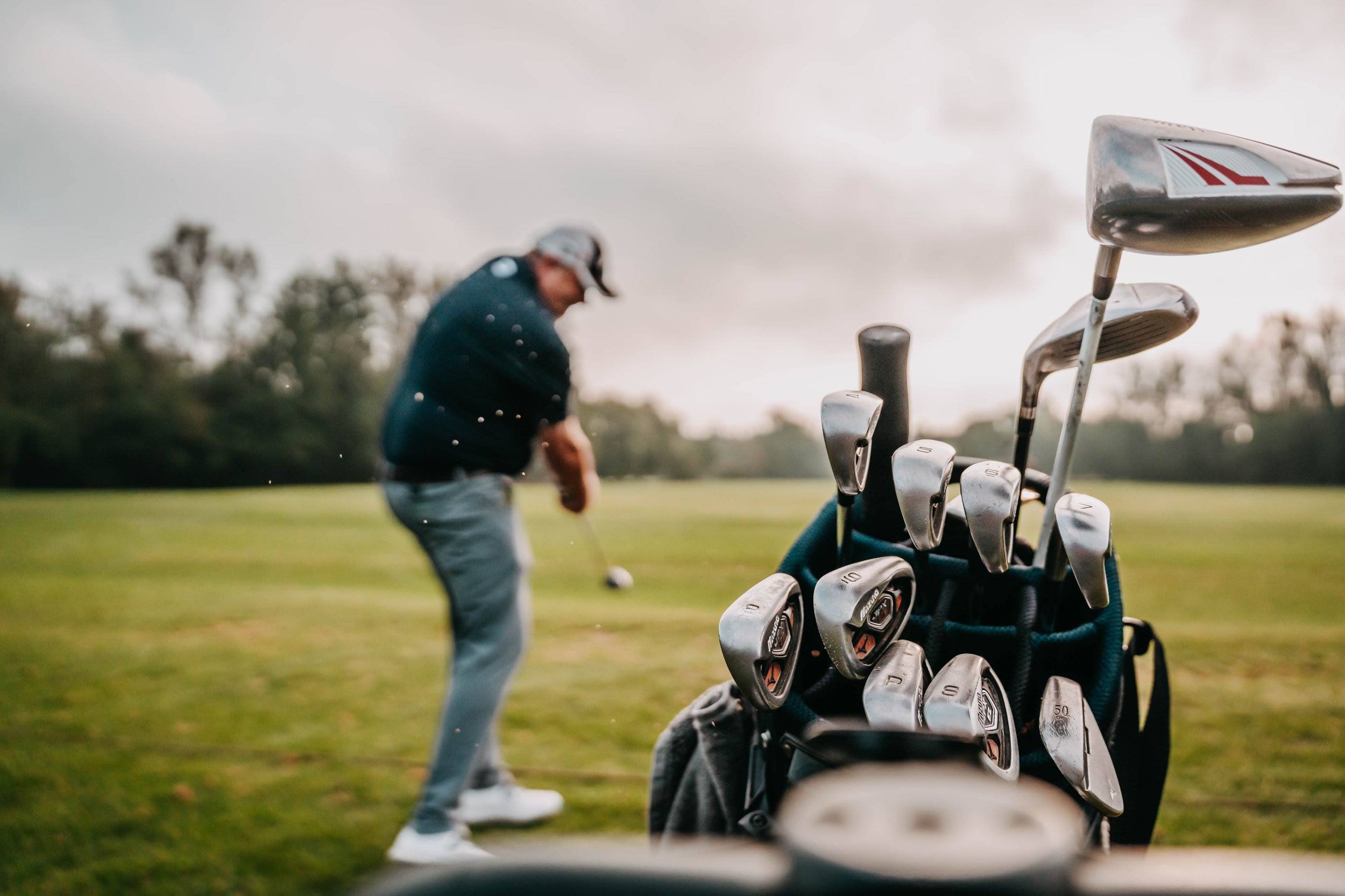 Golfer beim Schlag, im Vordergrund ein Golfbag mit Schlägern.